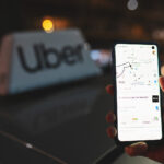 Uber app displayed on smartphone screen in front of the Uber taxi